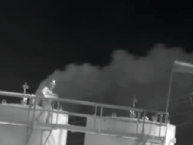Oil and gas industry worker on tank catwalk and inside gas leak from open thief hatch.