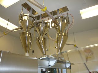 A sanitary vacuum conveyor keeps a tablet press filled in a pharmaceutical environment.
