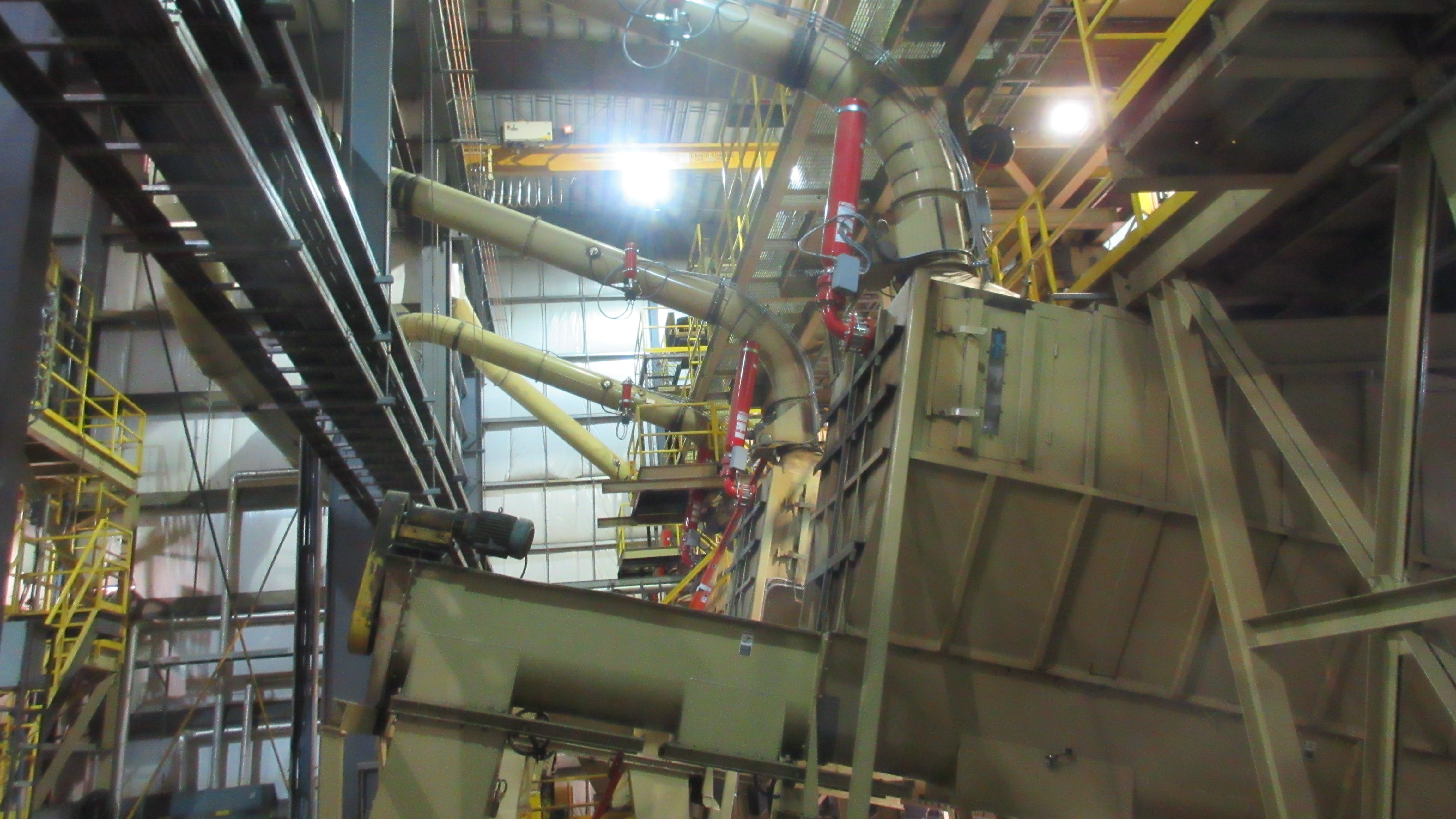 A hammermill with attached plenum is shown with remote dust aspiration and attached chemical suppression bottles that rapidly release chemical suppressant to extinguish fire in its early stages inside the mill when triggered.