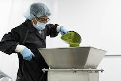 An operator empties a scoop of hand-weighed powder into the mixer intake which remains stationary as the vessel turns. An operator empties a scoop of hand-weighed powder into the mixer intake which remains stationary as the vessel turns.
