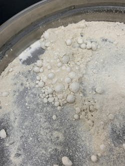 Figure 2. Macro image illustrating the tendency of fine powders to form low-density agglomerates that bridge or obstruct sieve apertures due to dry screening. Such behavior can bias particle size distributions by preventing accurate passage through smaller mesh sizes. Figure 2. Macro image illustrating the tendency of fine powders to form low-density agglomerates that bridge or obstruct sieve apertures due to dry screening. Such behavior can bias particle size distributions by preventing accurate passage through smaller mesh sizes.